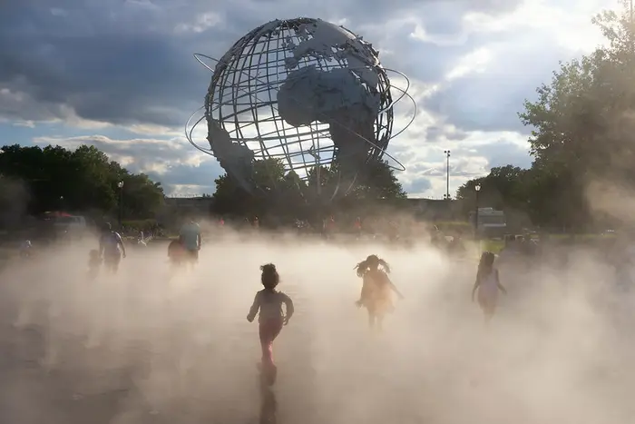 A group of young kids run through mist at the globe fountain in Flushing Meadows Corona park.